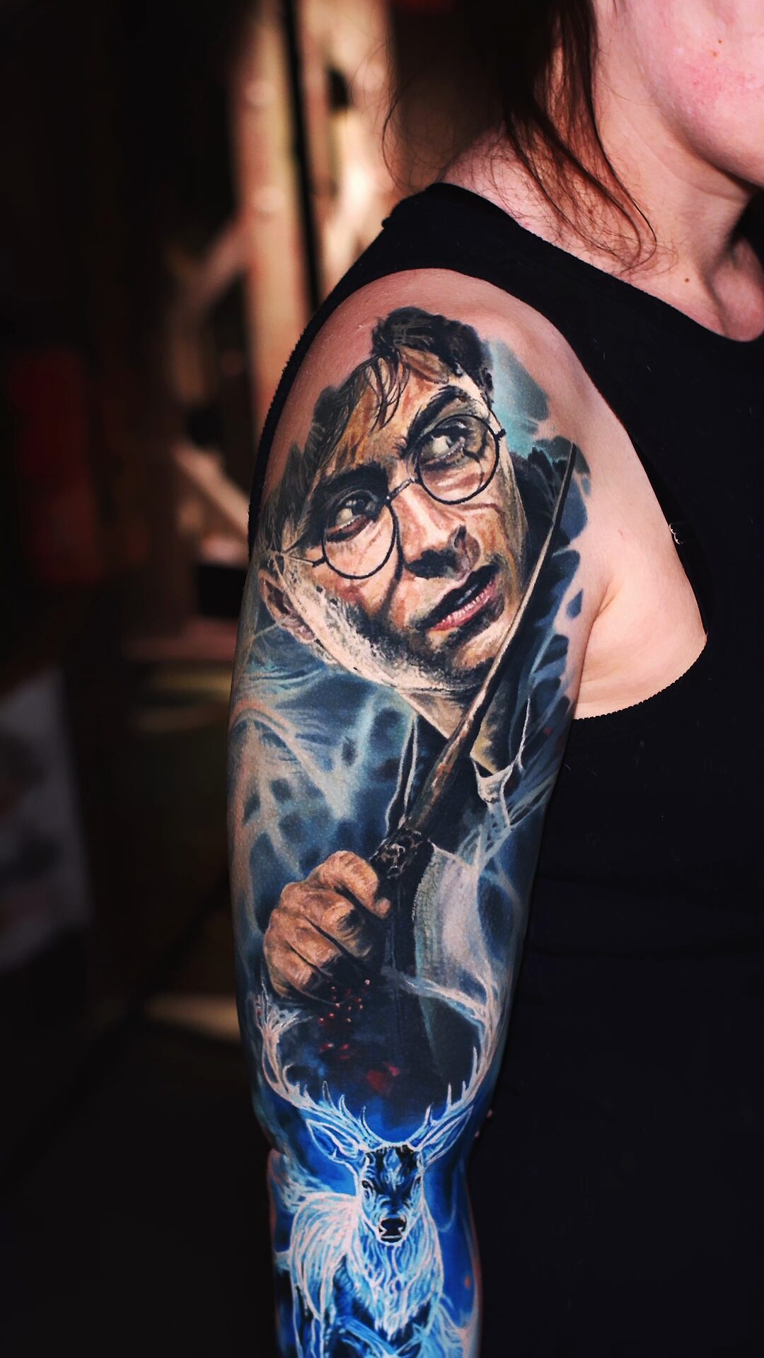 Color realism tattoo by Alex666cold — a realistic Harry Potter with raised wand and a glowing stag Patronus, arm and forearm